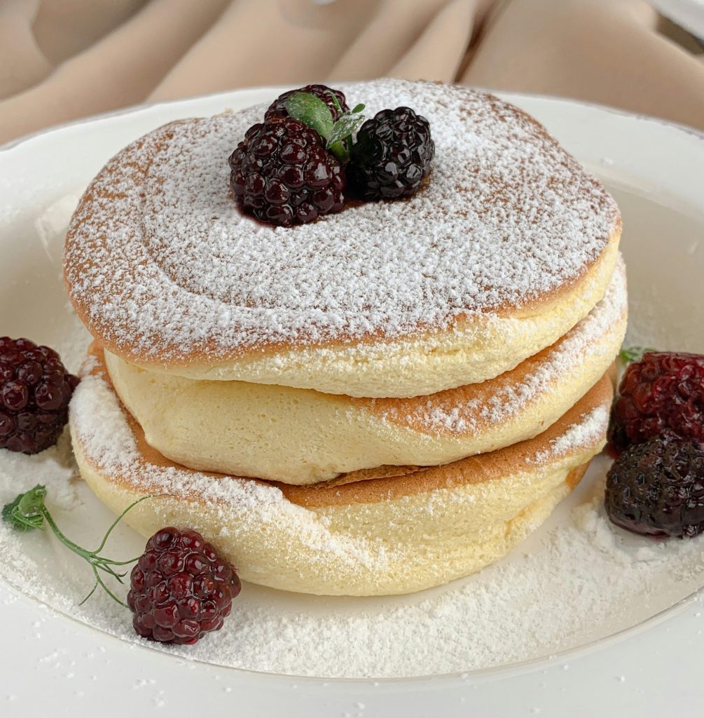 Delicious fluffy Japanese pancakes topped with blackberries and powdered sugar, perfect for a sweet breakfast.